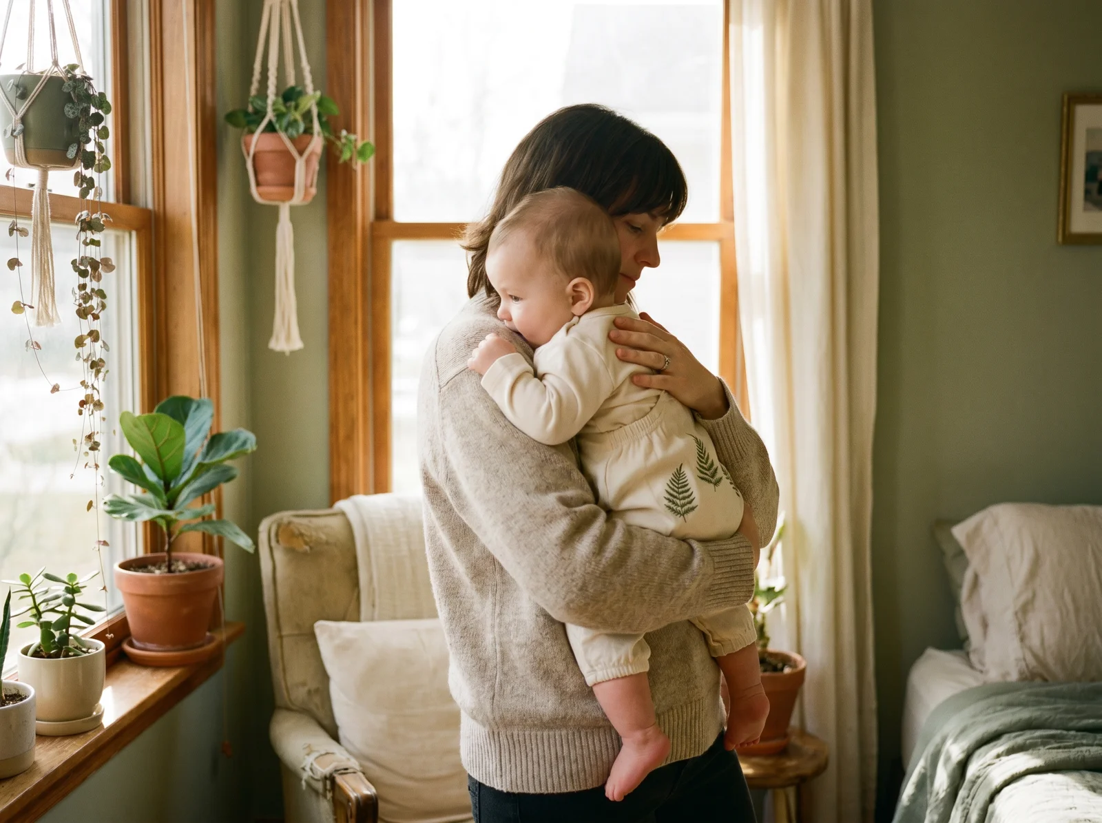 Parent holding a baby wearing a cream organic cotton romper with embroidered fern leaves